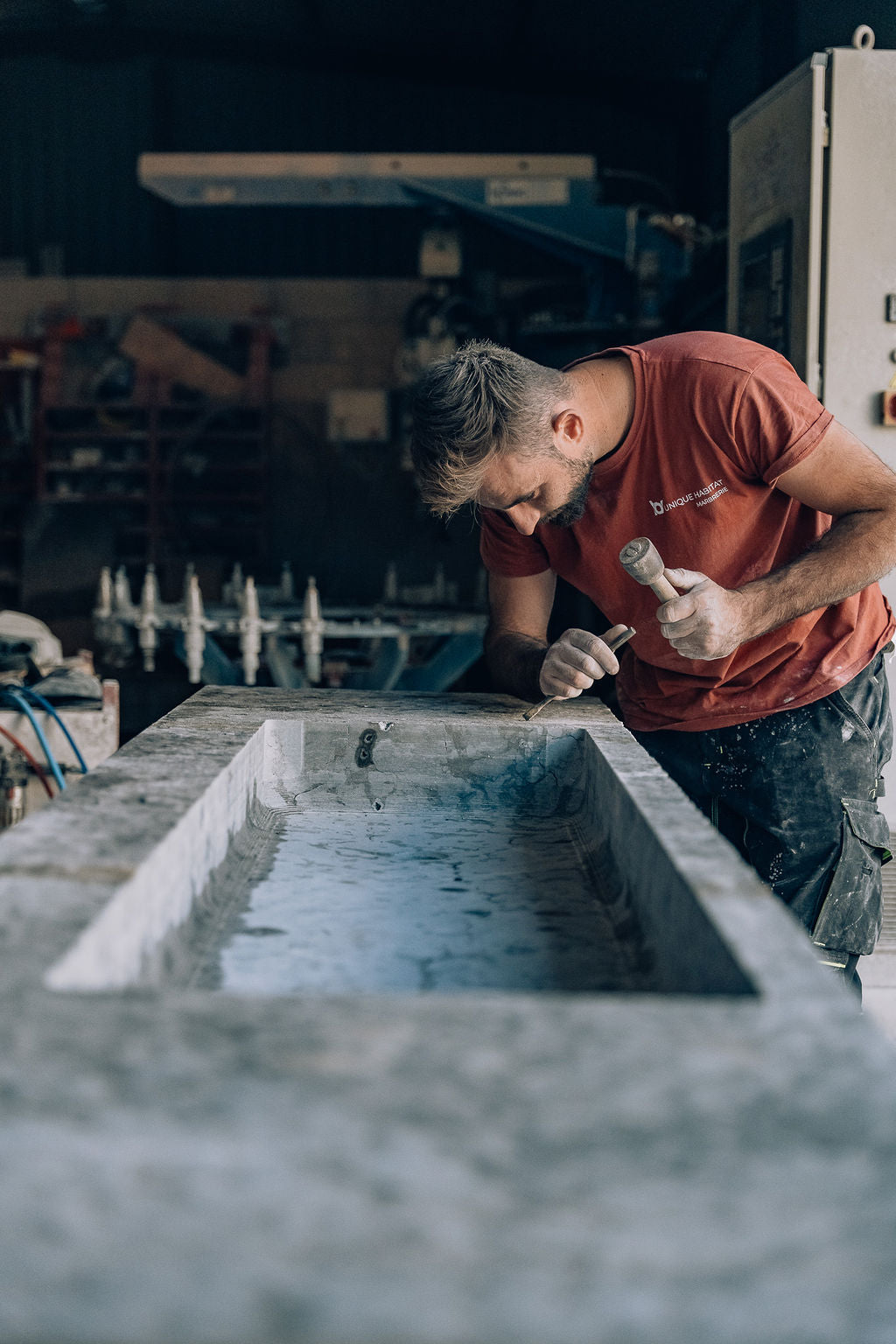 Artisan tailleur de pierre façonnant à la main une vasque en pierre naturelle dans l'atelier Unique Habitat