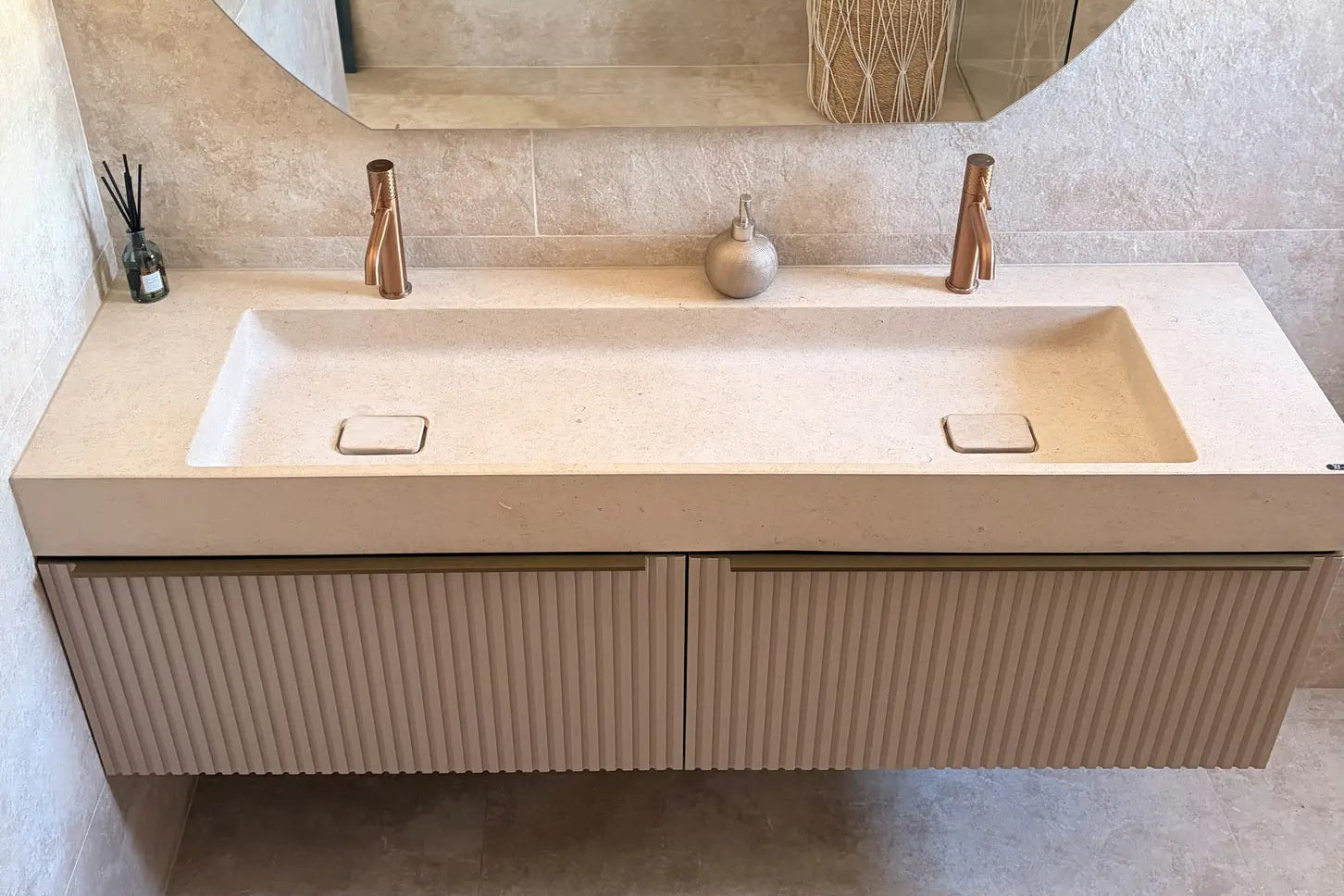 Plan vasque en pierre beige naturelle crème Moléanos, double cuve intégrée suspendue, bonde Magique en pierre, meuble cannelé, robinetterie cuivre, grand miroir rond, salle de bain contemporaine