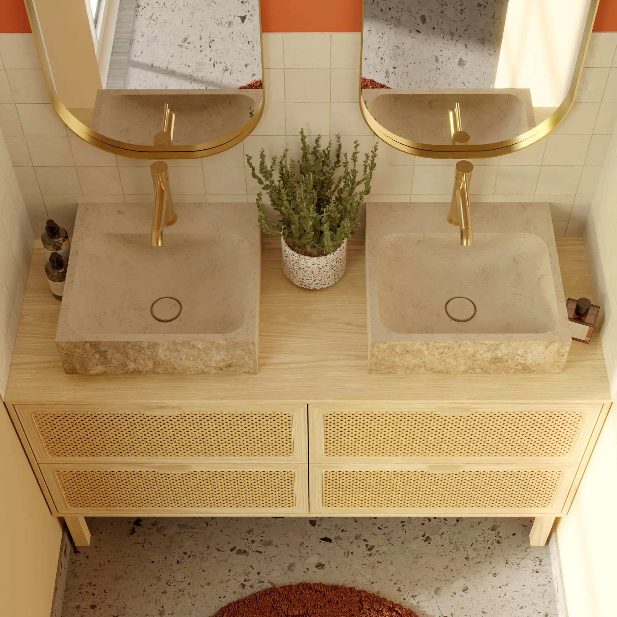 Salle de bain méditerranéenne avec double vasque à poser minimaliste en pierre naturelle crème Moléanos, contour brut et cuve polie, bonde Magique en pierre, robinetterie dorée, miroirs ovales dorés, meuble en bois clair et cannage, mur orange terracotta