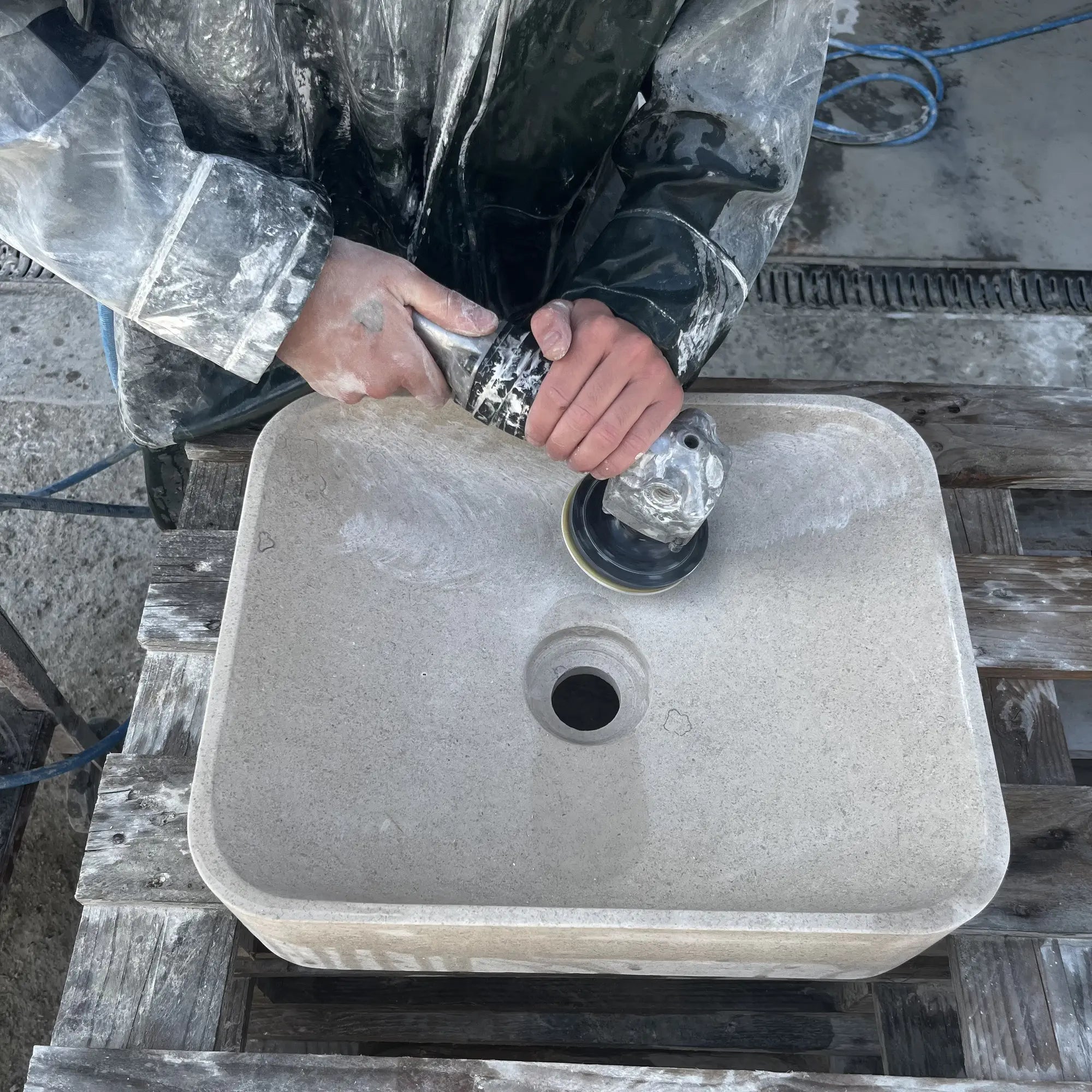 Artisan polissant à la main la cuve d'une vasque carrée en pierre naturelle crème dans l'atelier Unique Habitat, ponçage à la disqueuse, fabrication artisanale française