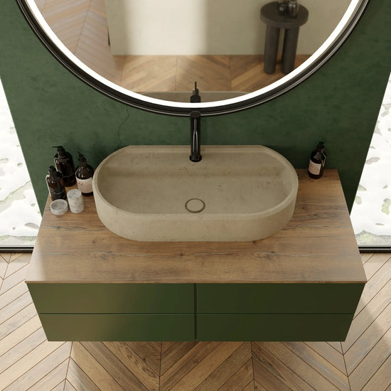 Vasque à poser ovale design en pierre naturelle crème Moléanos, bonde Magique en pierre, robinetterie noire, meuble suspendu vert à plan en bois, miroir rond LED, mur vert et parquet chevron, salle de bain contemporaine