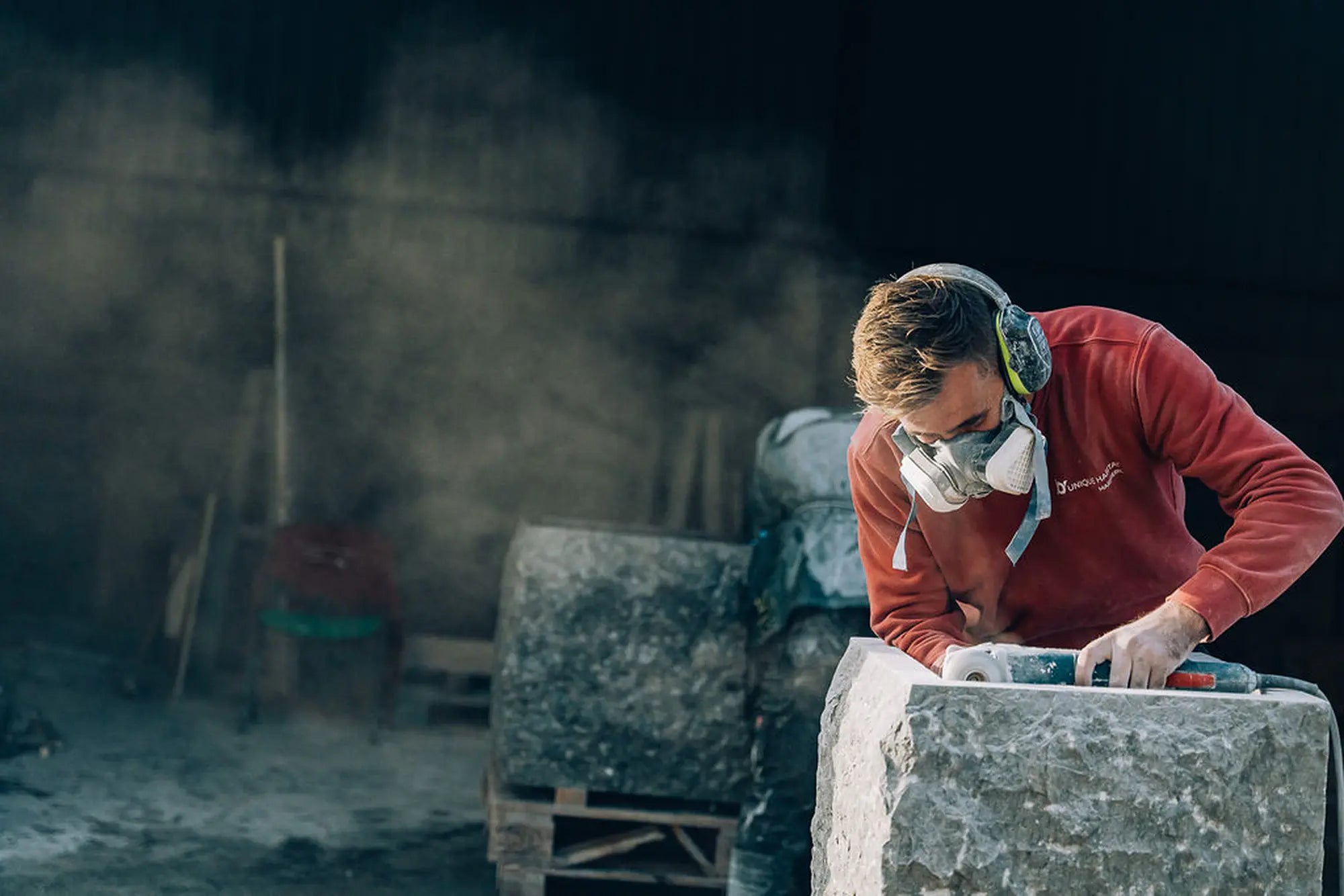 Artisan Unique Habitat sculptant un bloc de pierre naturelle pour une vasque ovale dans l'atelier, masque et casque de protection, poussière de taille, fabrication artisanale française