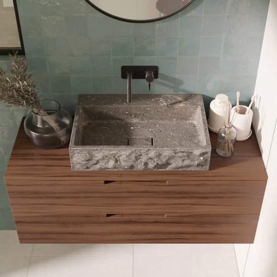  Vasque à poser rectangulaire minimaliste design en pierre naturelle bleu gris San Vicente, contour brut et cuve polie, bonde Magique rectangulaire en pierre, robinetterie murale noire, meuble suspendu en bois foncé, miroir rond noir, mur en zellige vert d'eau, salle de bain contemporaine